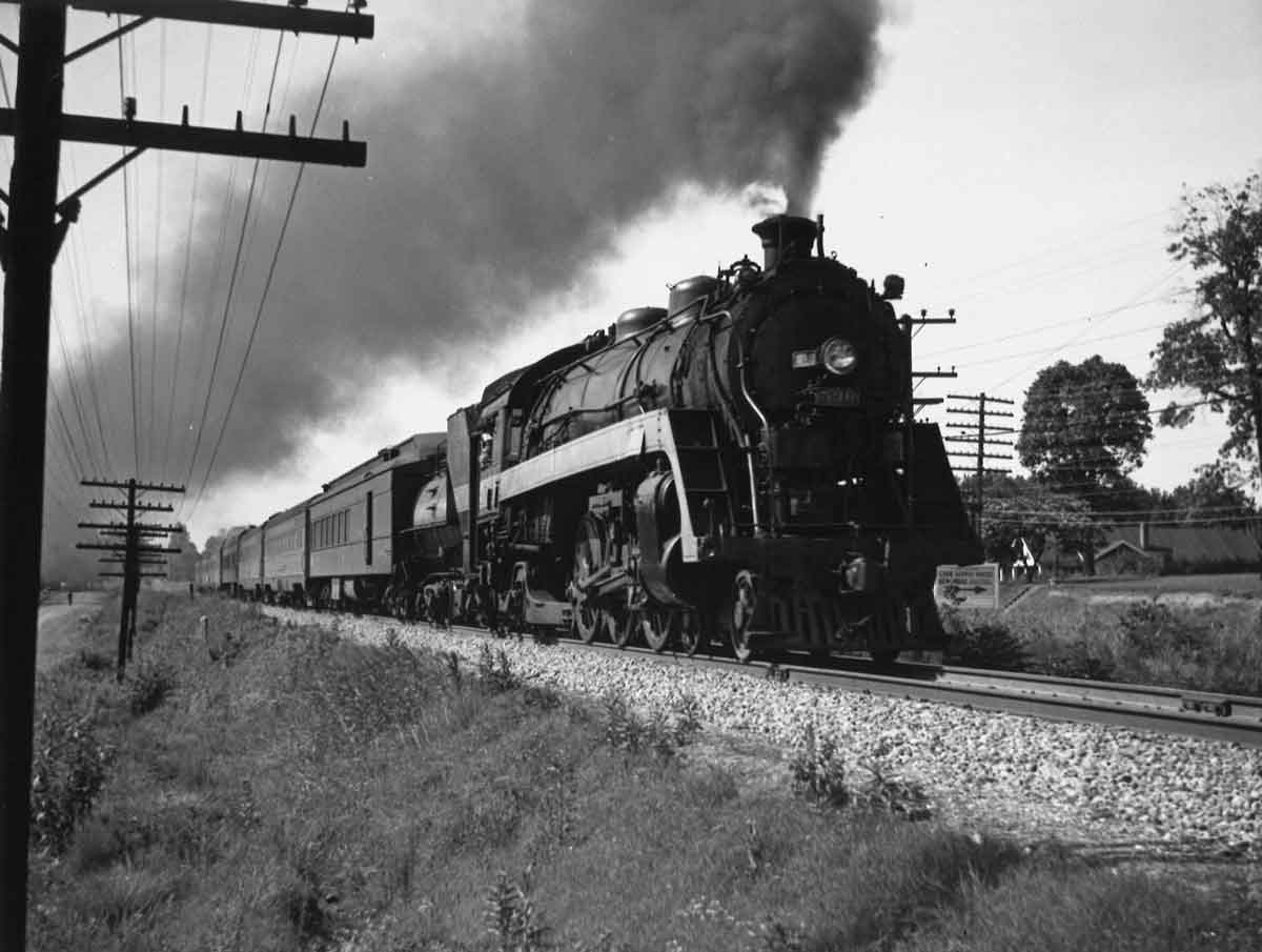 A black and white photo of a train passing through a rural town