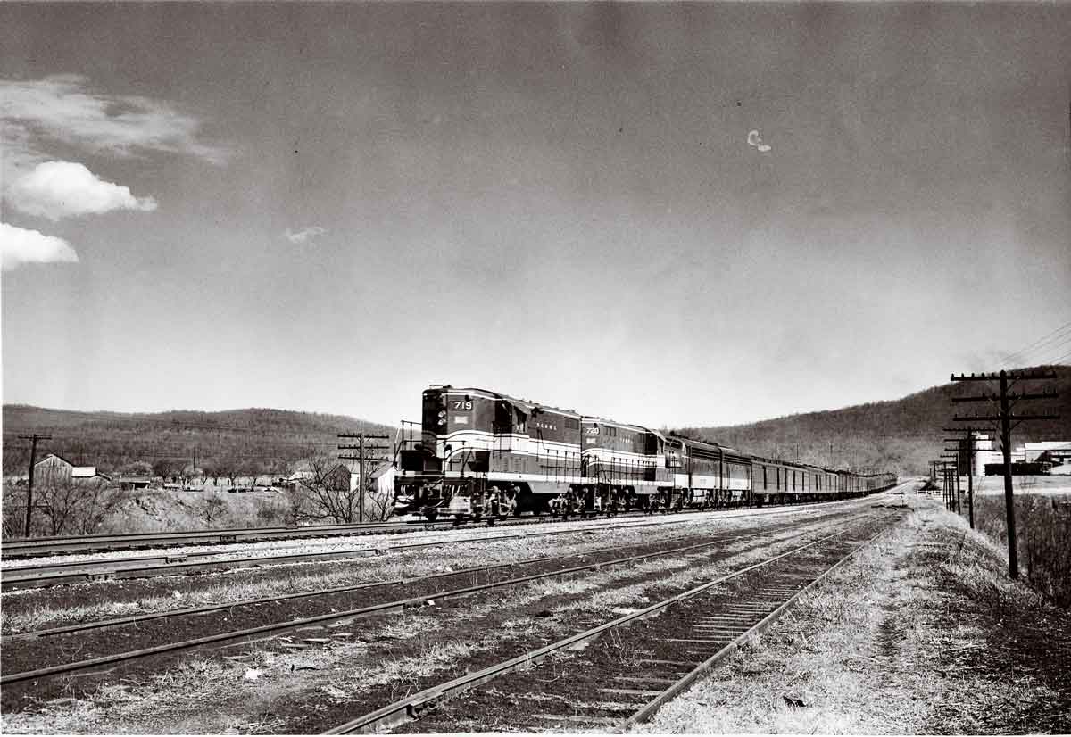 A black and white distant shot of a train passing through a rural area