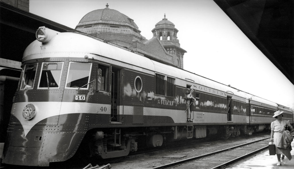 A lady walking by a train parked in a train station