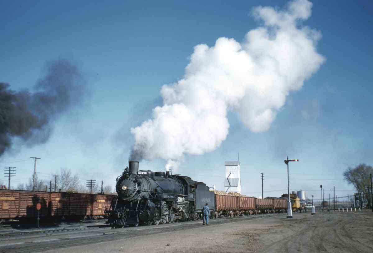A train passing by with big white smoke coming out of its chimney