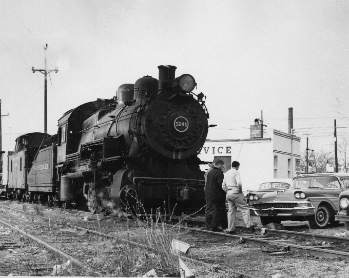 Men look over automobile in front of locomotive