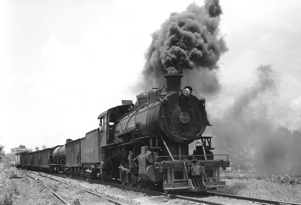 A black and white photo of 2-8-0 Consolidation 312 coming down the tracks with black smoke coming out of its chimney