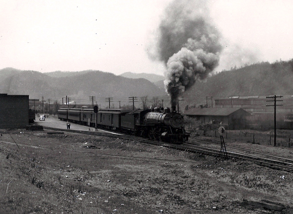 A black and white photo of Clinchfield 4-6-2 with smoke coming out of the chimney passing through buildings
