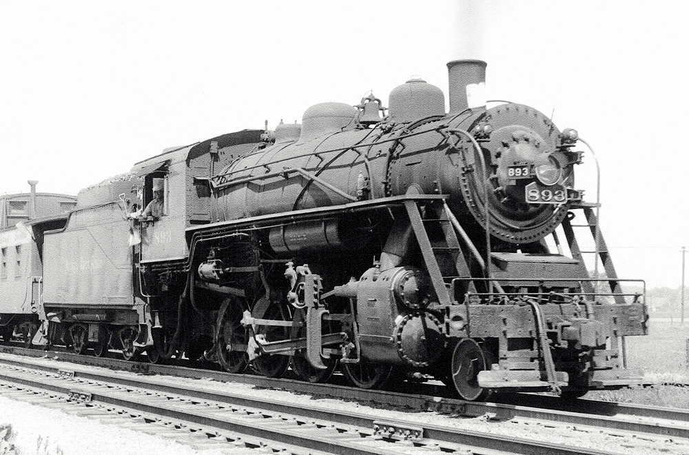 A close up black and white photo of a 2-8-0 Consolidation-type steam locomotive with the conductor looking out the window