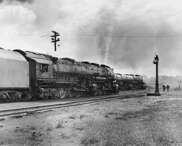 A train passing by a stop light and two people walking