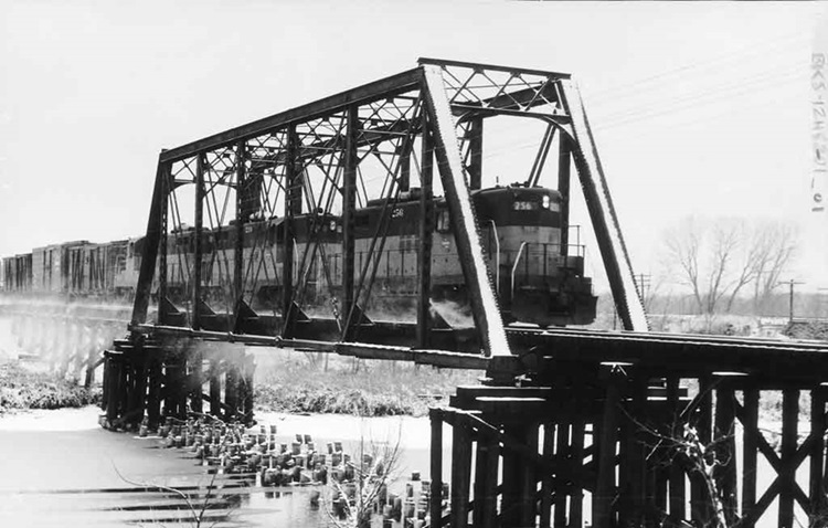 Three diesel locomotives with freight train on bridge in snow