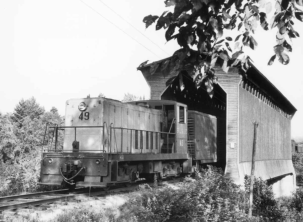 Diesel switcher locomotive exits wooden covered bridge with train