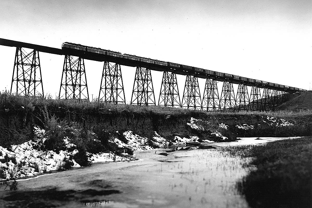 Diesel locomotives pull a long freight train over a high bridge.