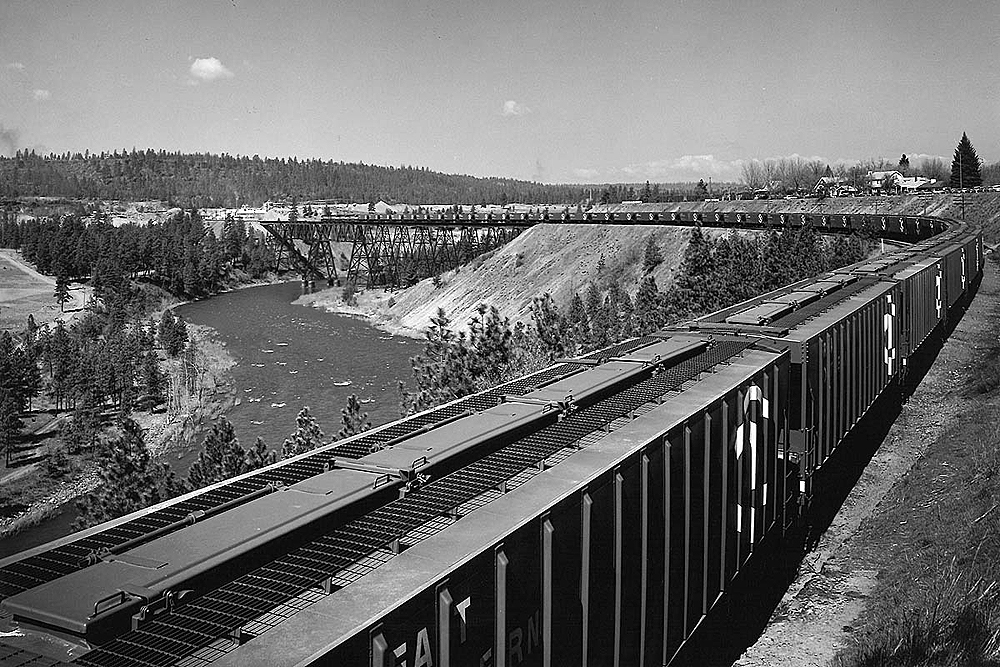 Covered hopper train on a mountain plateau crossing a bridge and river.