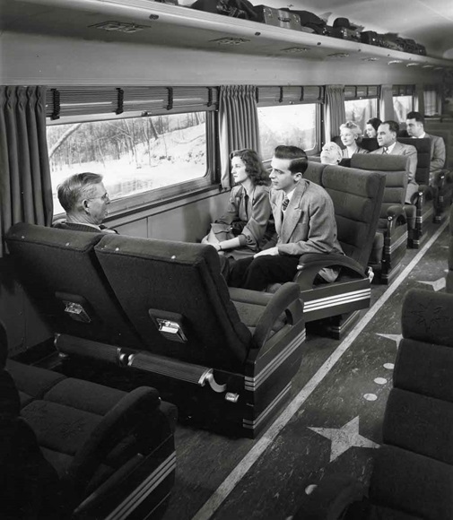 Several people in cloth cushioned bench-style coach seats looking out a passenger coach on a snowy scene.
