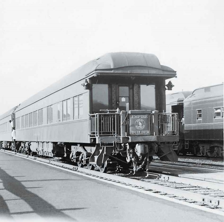 The tail of an observation car in a yard or station displaying an "Empire Builder" emblem on the rear.