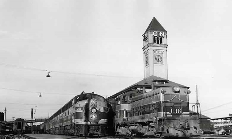 Several trains paused near a train station with large clocktower.