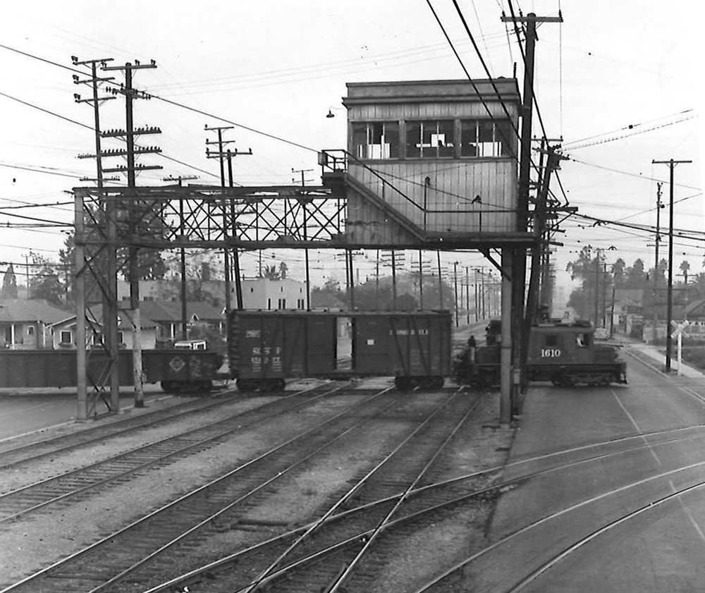 A freight cross a complicated track diamond just underneath a signal bridge.