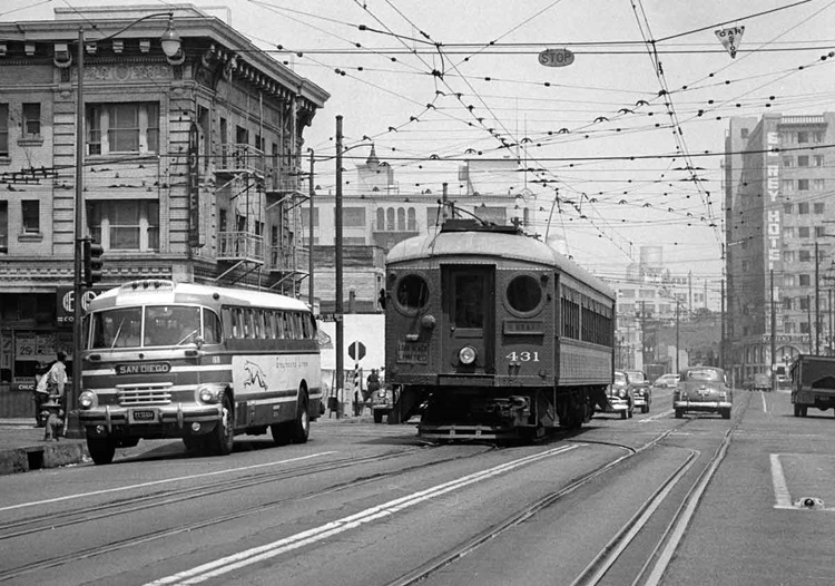 An interurban car operates in the middle of a busy downtown street.