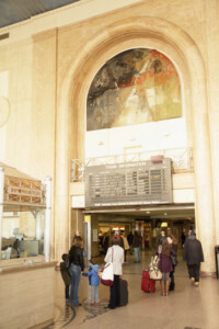 Large mural in an archway of a passenger station as passenger walk or stand nearby.