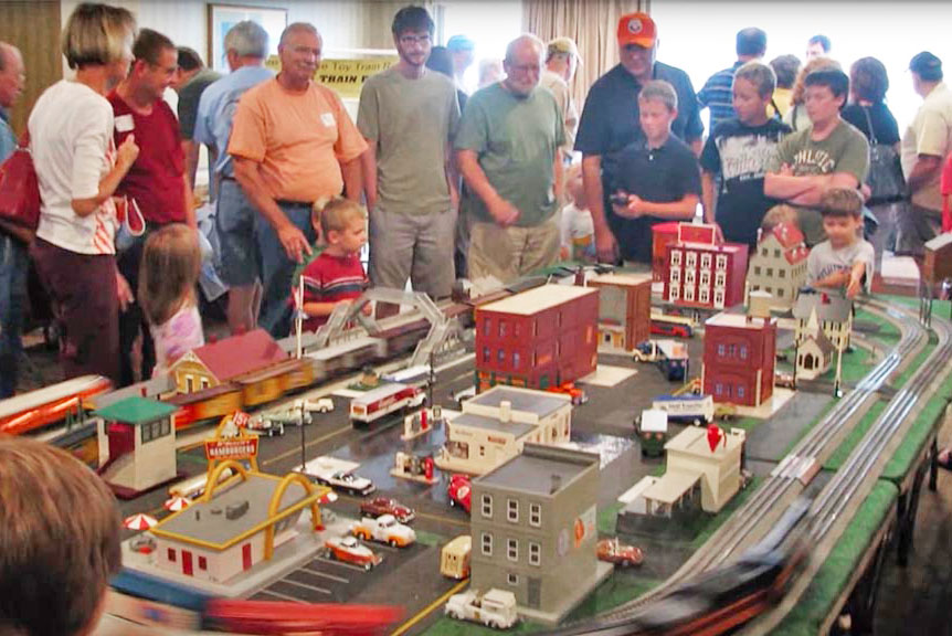 A group of people standing around an O gauge layout