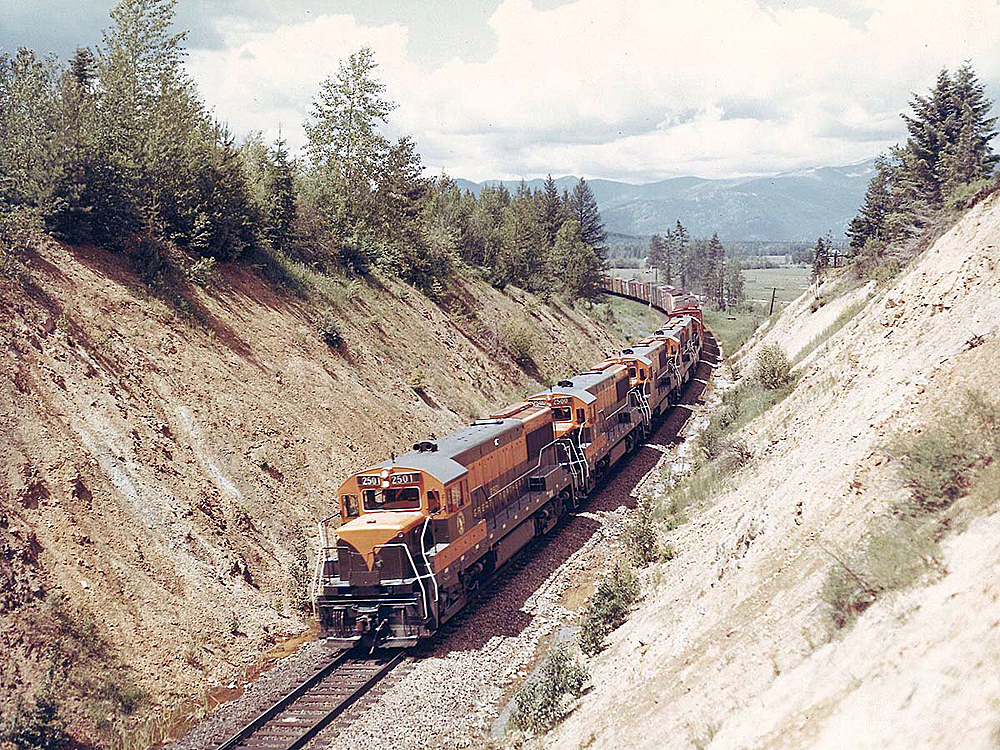 Four locomotives pull a freight train uphill.