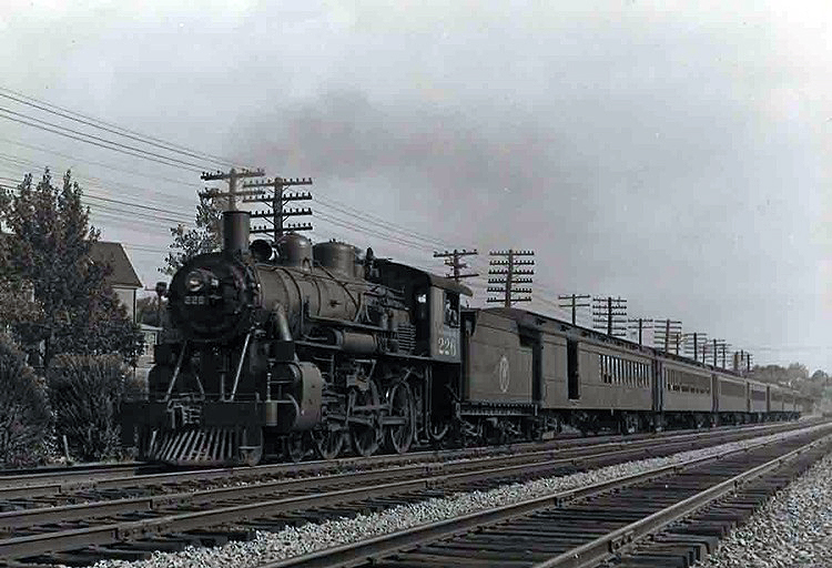 A steam locomotive leading a long passenger train over a multi-track mainline.