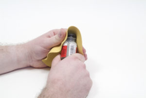 One hand wraps a rubber sheet around a paint cap while another hand holds the paint jar.