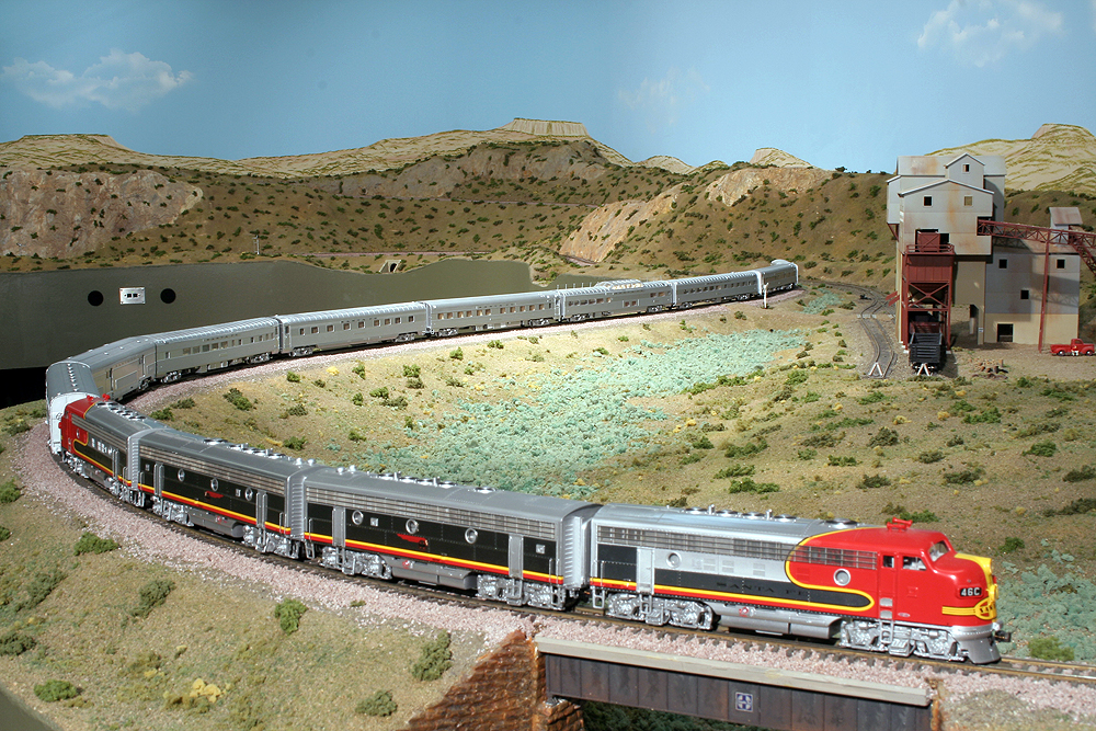 A sweeping photo of a silver-colored HO Scale Sante Fe streamlined passenger train pulled through a desert Southwest scene.