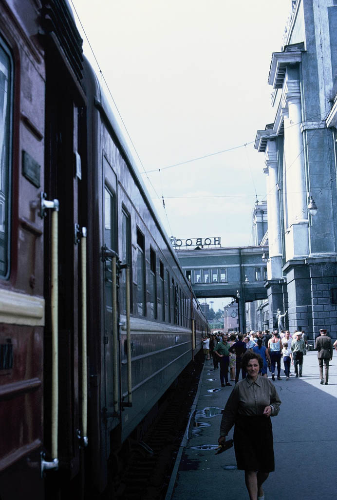A woman walks toward a camera alongside a train stopped a station.