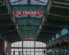 Green painted steel arches and a glass ceiling focused on "To Trains" sign.