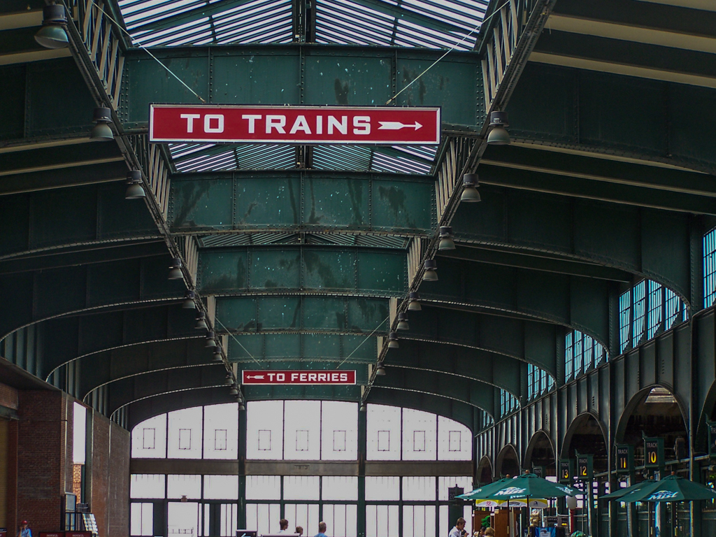Green painted steel arches and a glass ceiling focused on "To Trains" sign.