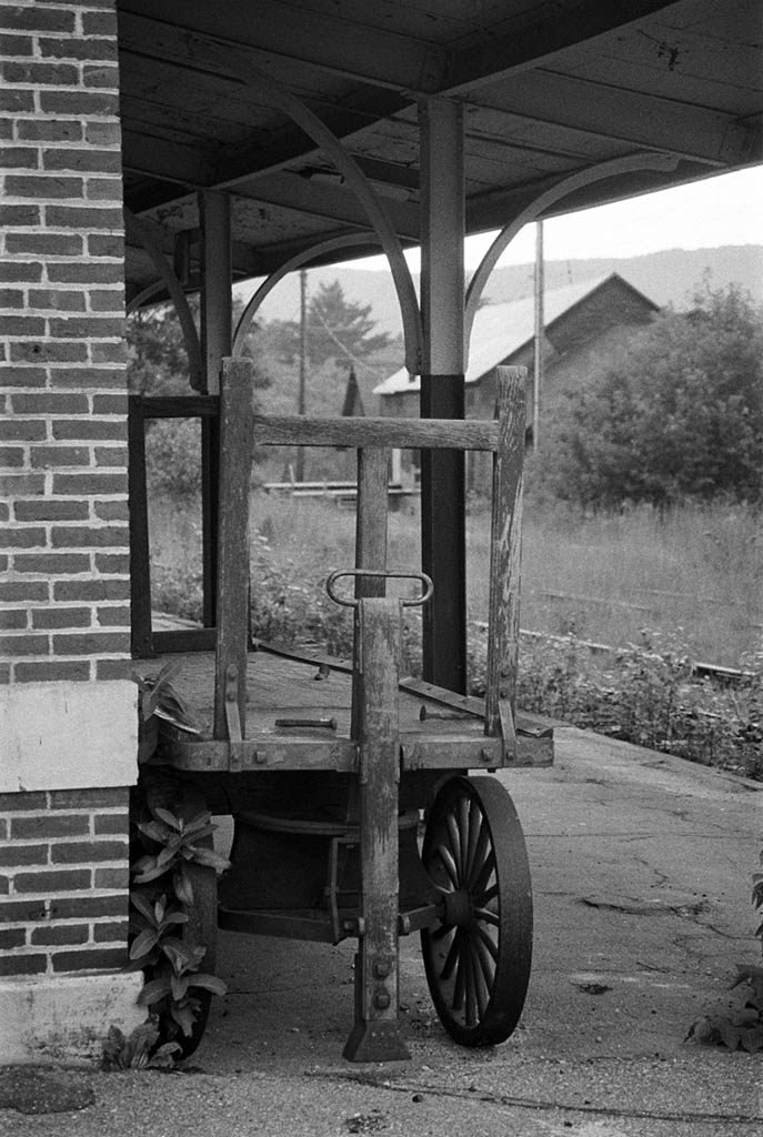 Black-and-white image of wooden baggage cart at an abandoned train station.