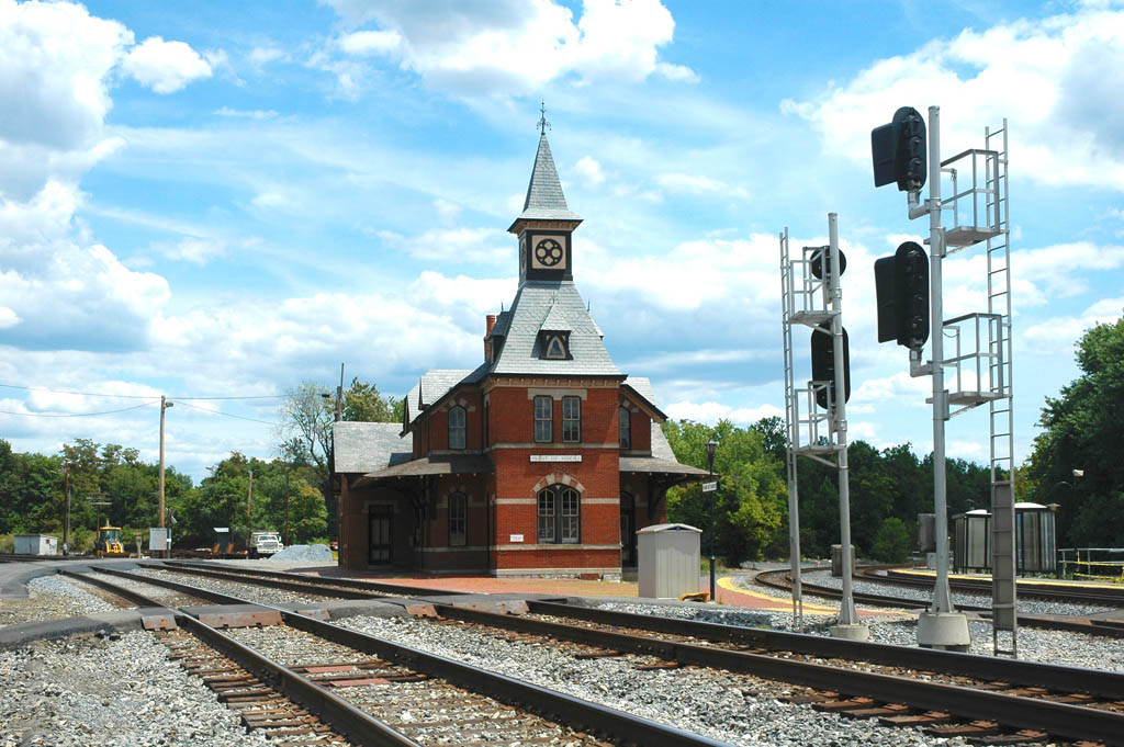 A gothic revival passenger train station at the junction of two double-track lines.