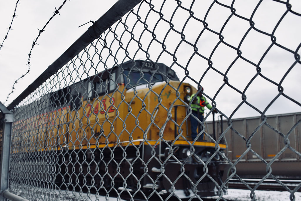 Yellow diesel locomotive behind a chain link fence on a cloudy day.