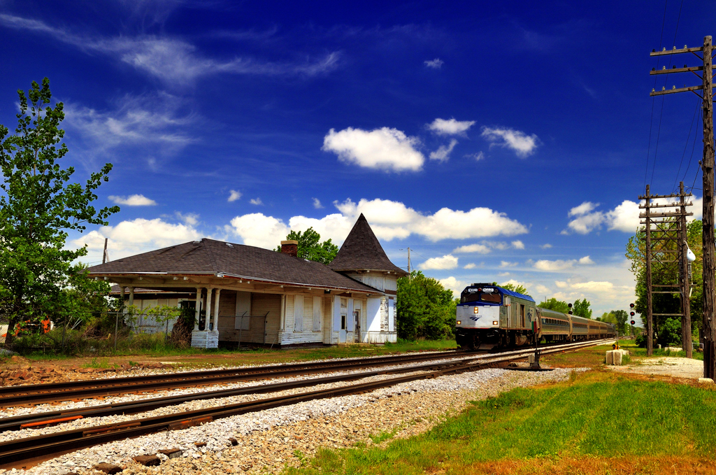 An Amtrak passenger train passes by an old and falling down train station.