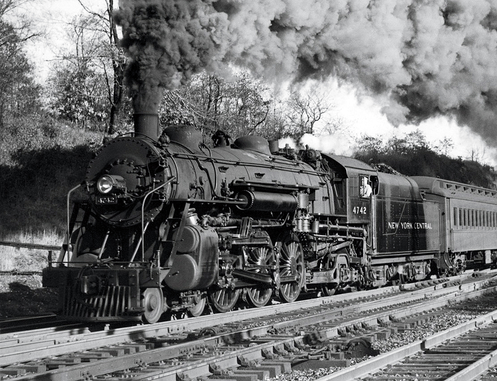 A steam locomotive hauling a passenger car on a multi-track mainline.