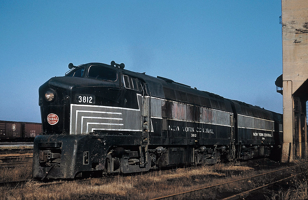 A black and silver "shark nose" diesel sits on a weedy track in a rail yard.
