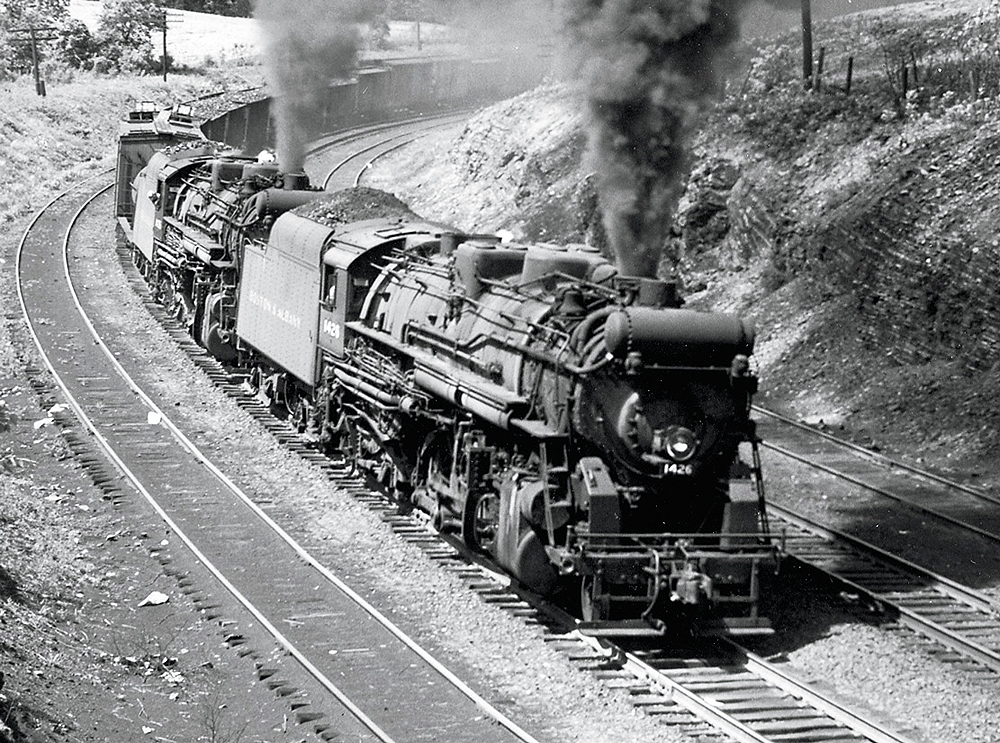 Two double-headed steam locomotives head around a curve hauling a freight train.