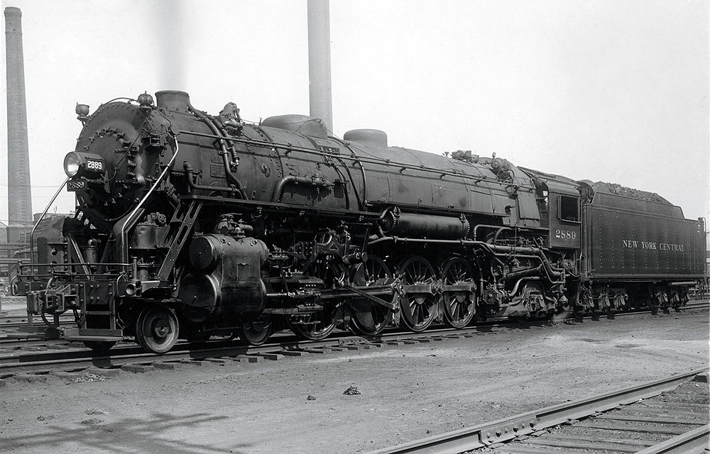 A large steam locomotives pauses in a rail yard.