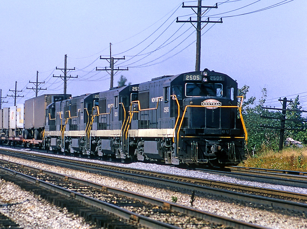 Four diesel locomotives coupled together haul a train on a multi-track main line.