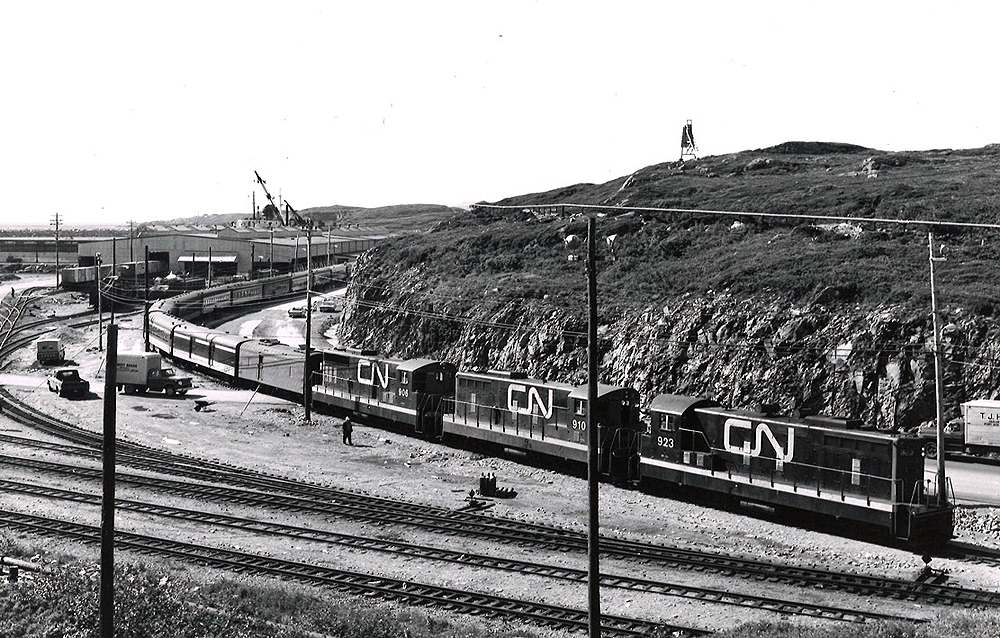 Three CN locomotives take the lead of a passenger train in a rail yard.