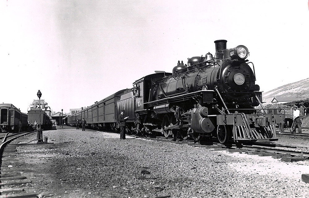Steam locomotive at the head of a passenger train in a rail yard.