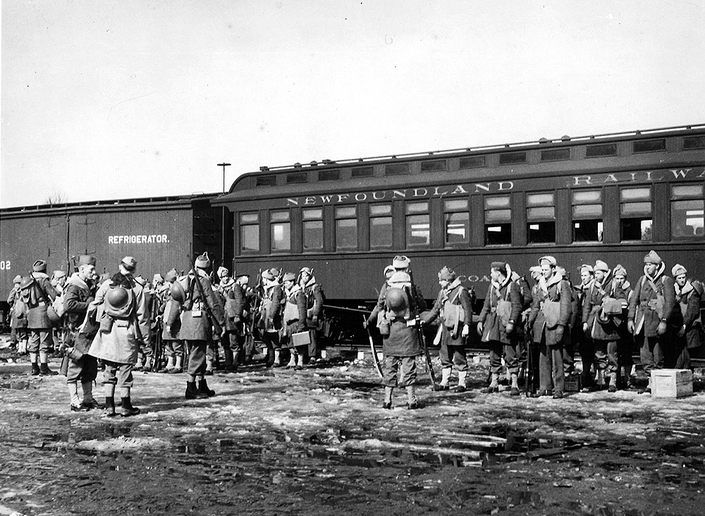 Soldiers in loose formation wearing what appears to be winter clothing in front of a mixed train.