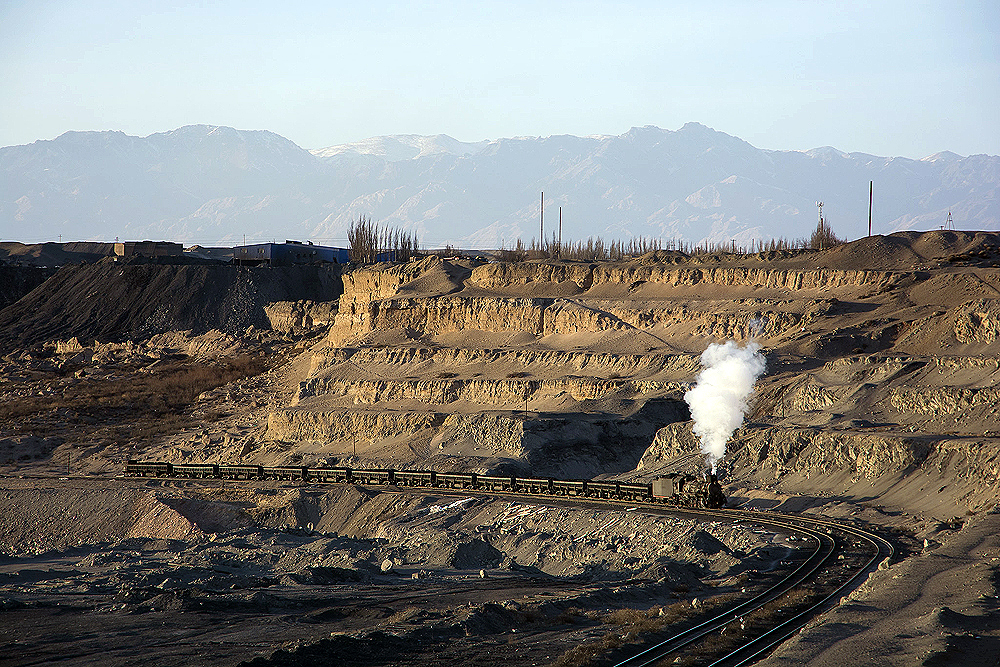 A steam locomotive hauls a short train through a mined area.