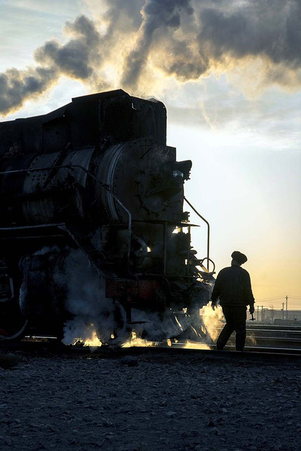 A silhouetted person in front of a steam locomotive.