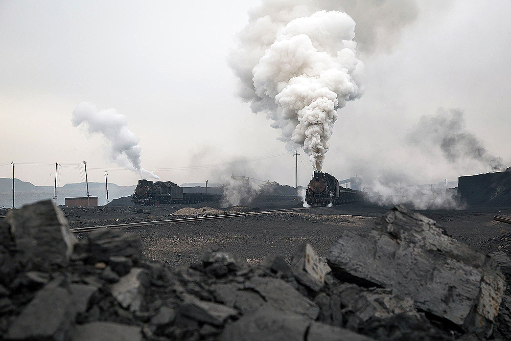 Loose lump coal in the fore ground frames two steam locomotives in an industrial rail yard.