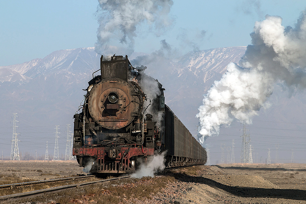 A steam locomotive hauls a train and seen in a classic North American three-quarter wedge image.