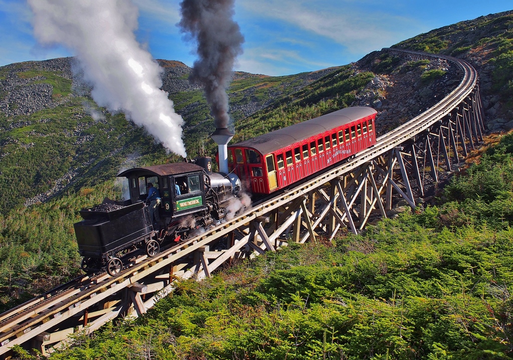 A geared funicular steam locomotive pushing a passenger car up a steep-inclined trestle.