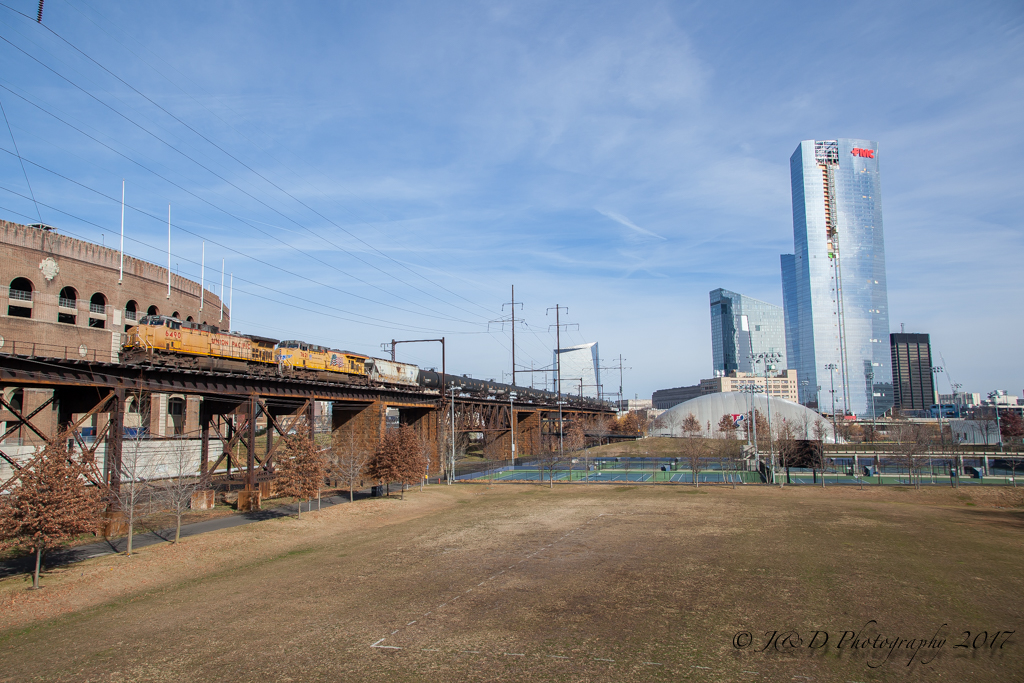 Yellow diesel locomotives hauling a tank car train on an elevated bridge.