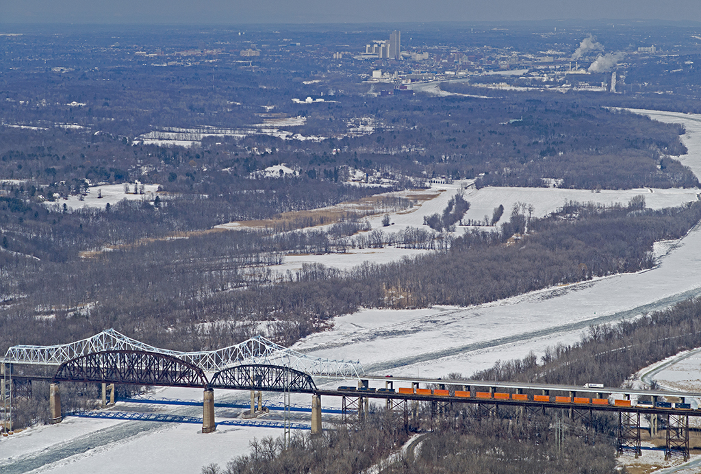 Overhead view of a train moving across a bridge above a frozen river in winter time.