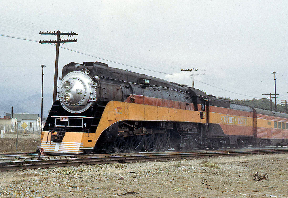 An orange-and-black steam locomotive at the head of a passenger train.