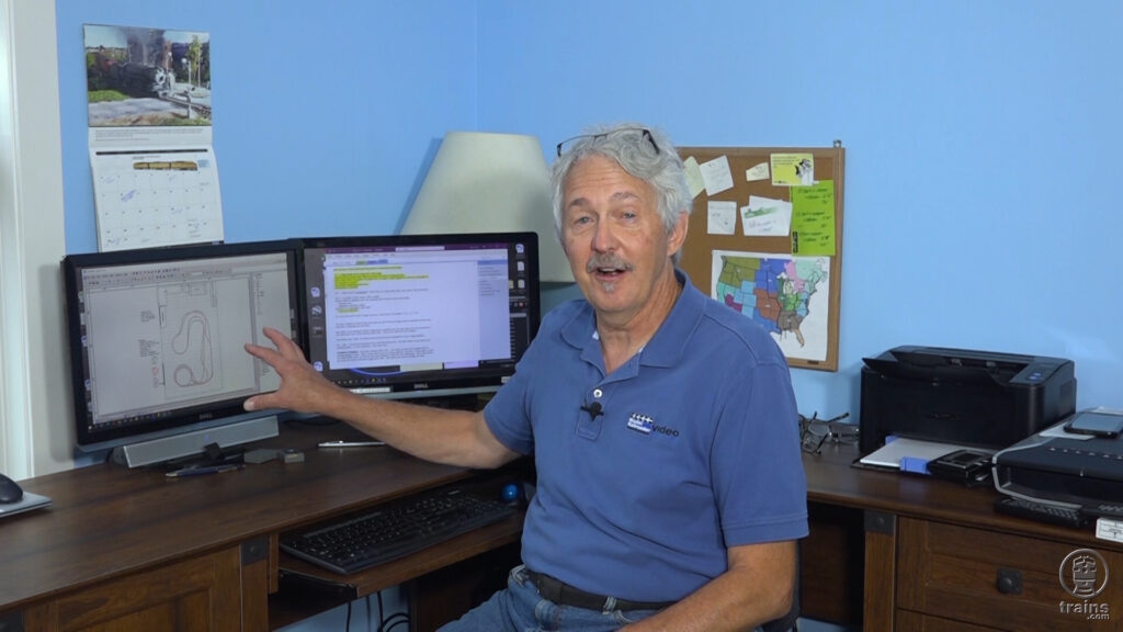 Gerry Leone sitting at his desk and pointing to a track plan on his computer screen