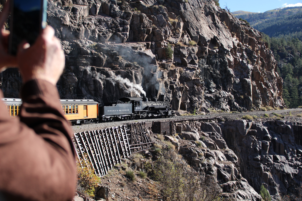 A steam locomotive-hauled passenger train navigating a rocky slope as seen from a car in the rear of the train.