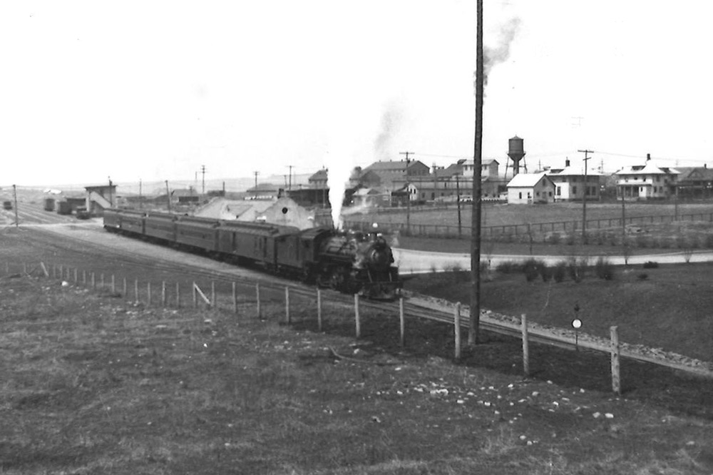 Steam locomotive with passenger train at station.
